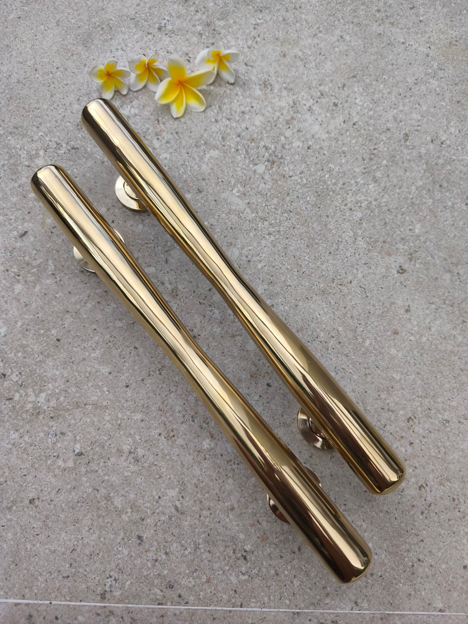 Two polished brass door pulls laid diagonally, long gold bar handles with a modern tapered shape for front doors, gates and interior doors
