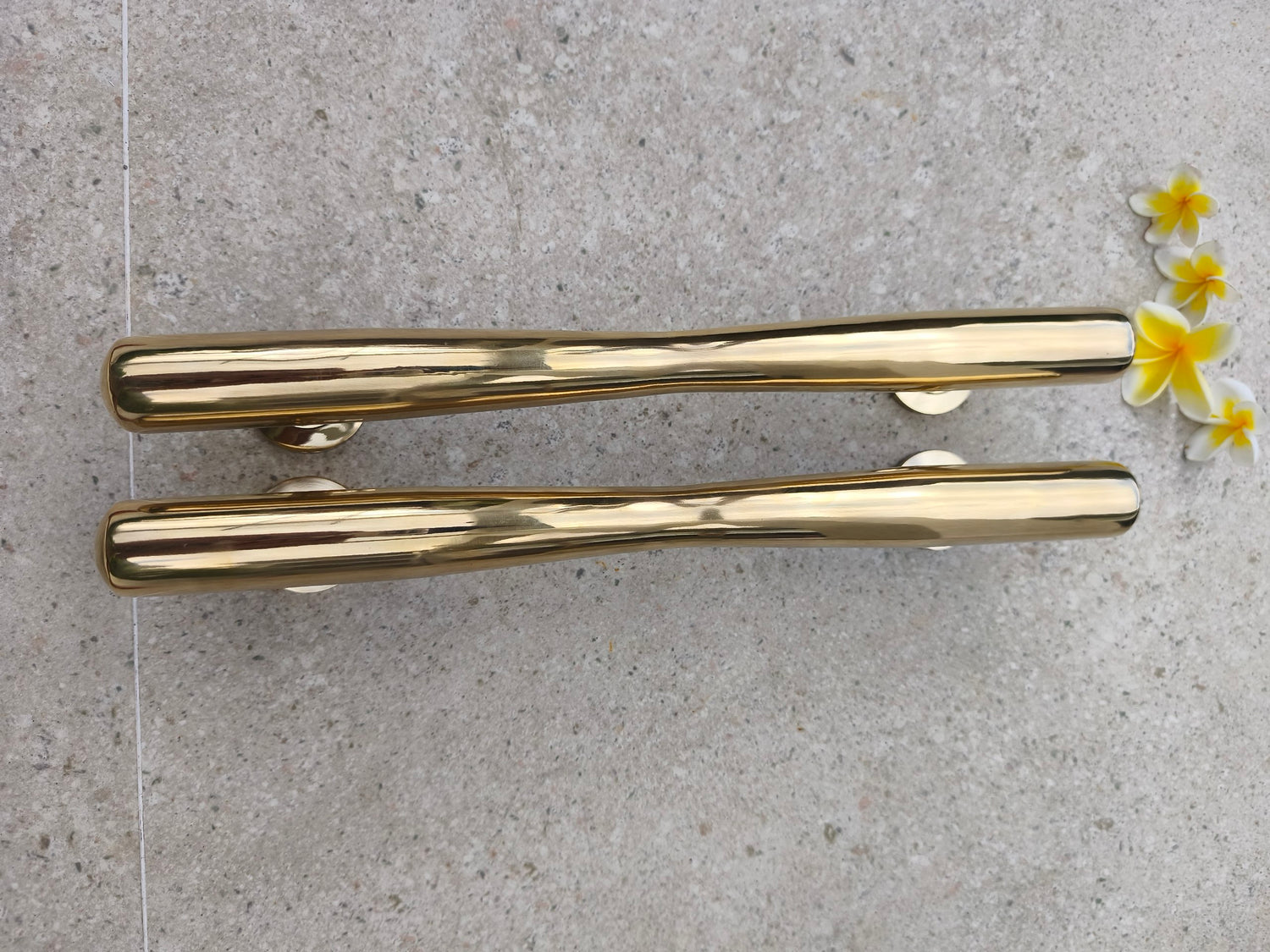 Close up profile of polished brass door pulls showing the smooth tapered bar and mounting posts, durable solid brass door hardware