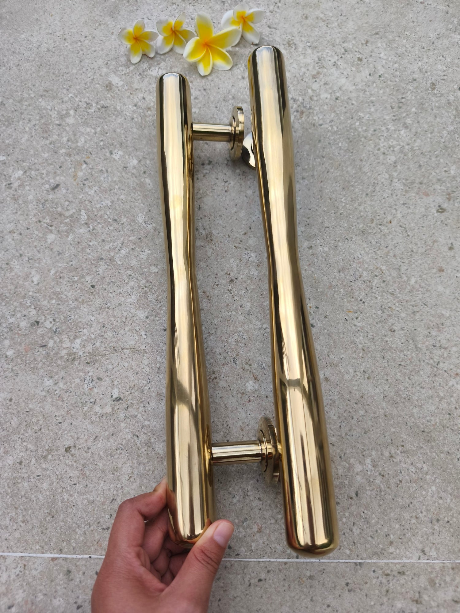 Hand holding a pair of solid brass door pulls upright, polished gold tapered handles for double entry doors, barn doors and large wooden doors