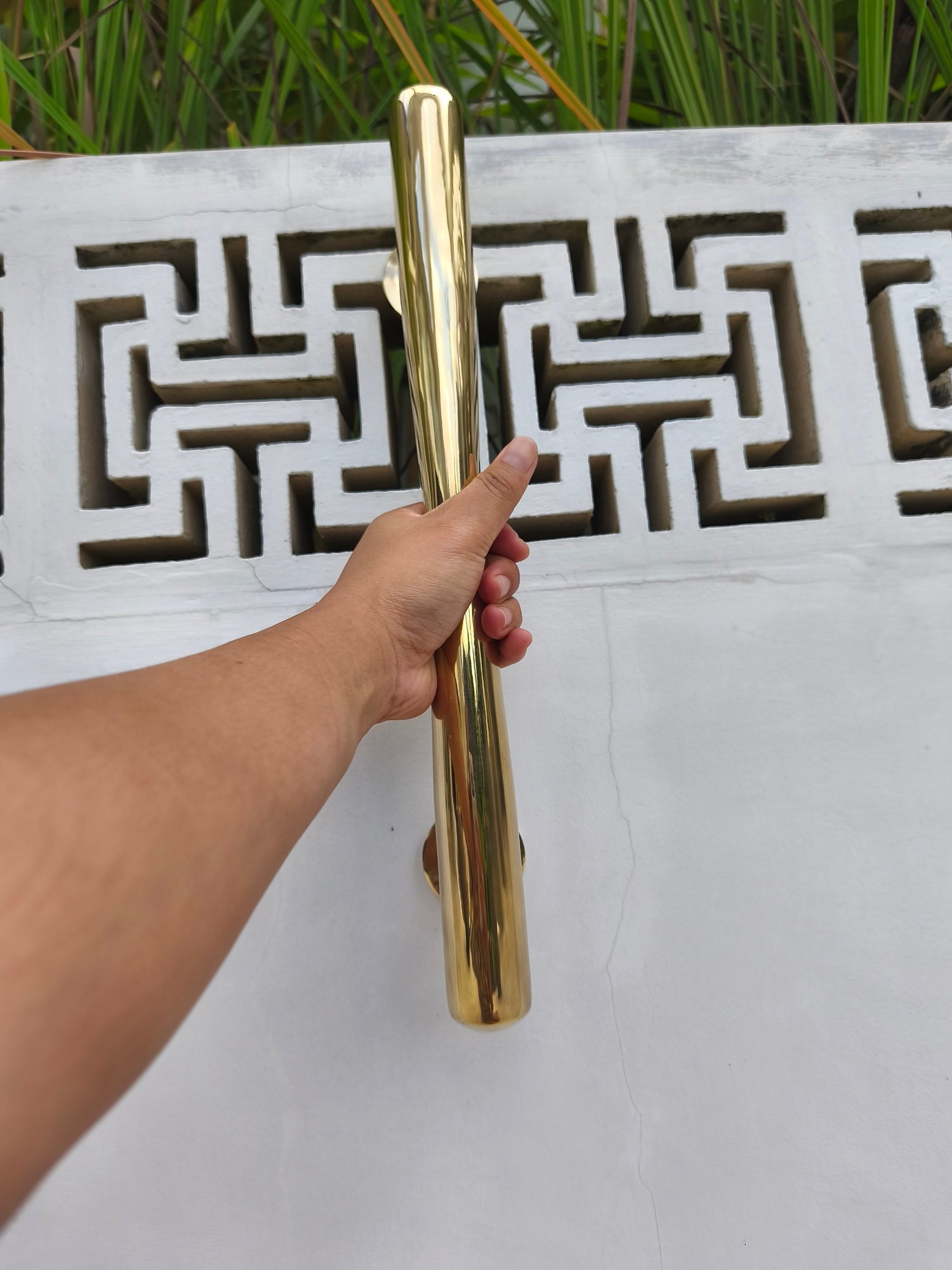 Hand holding a polished brass door pull against a white patterned wall, long gold entry door handle that suits modern and classic home styles