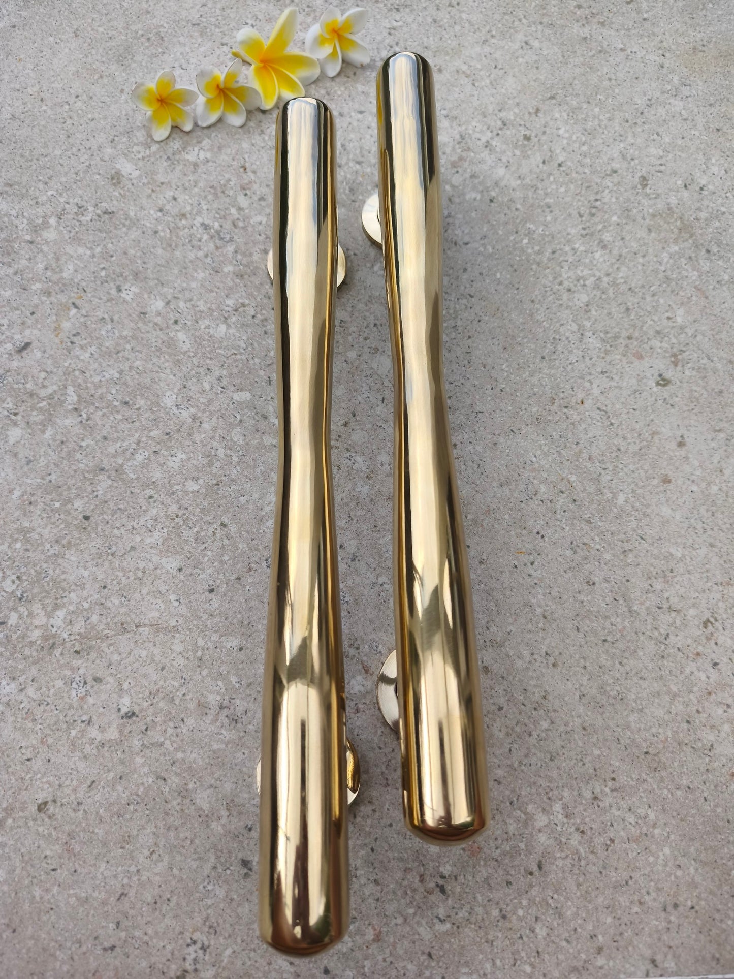 Close up of two polished gold brass pull handles, solid brass door hardware with a smooth finish that develops a richer gold tone over time
